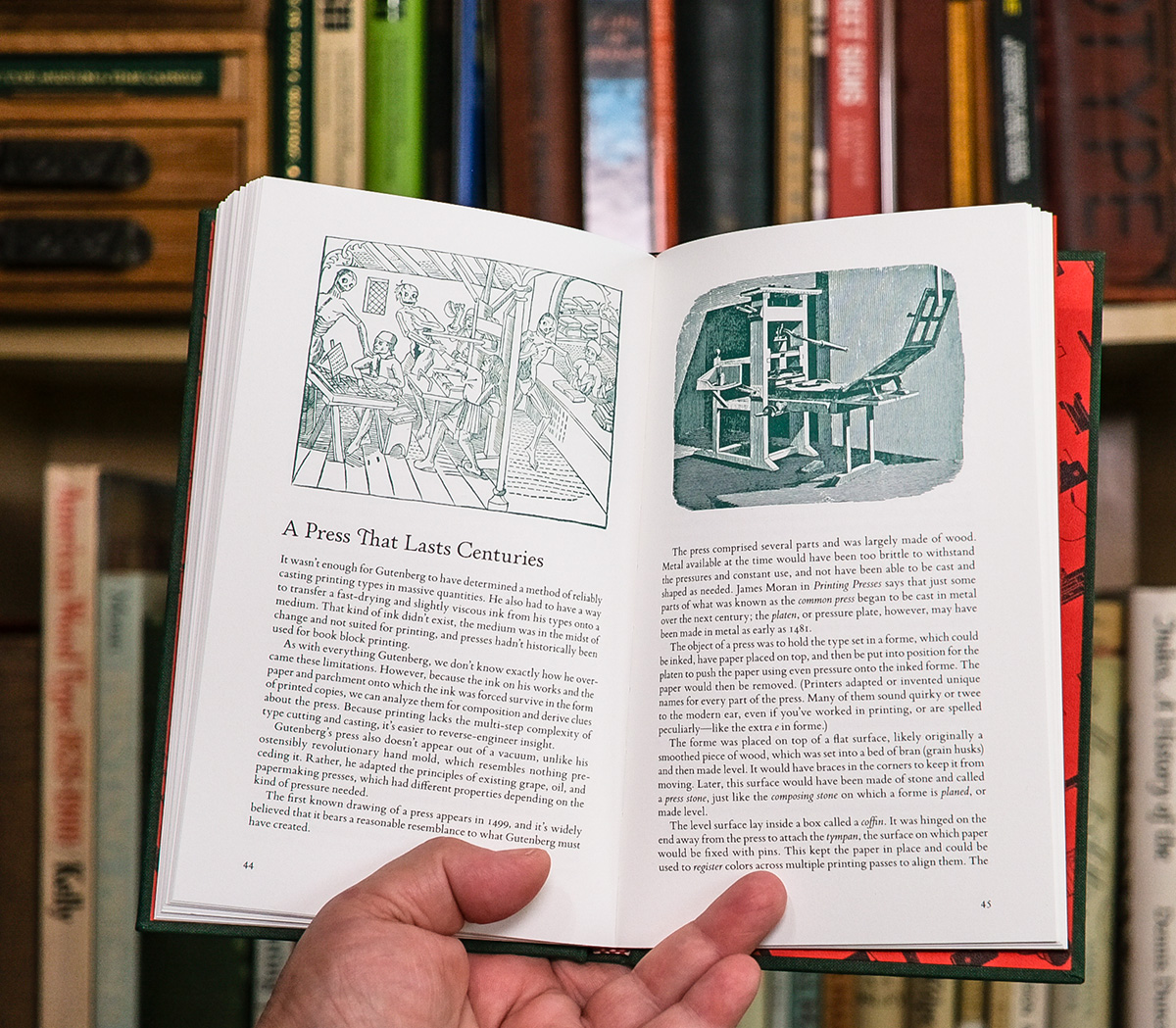 Two-page spread from the book showing two illustrations in green at the top of each page. Hand holds the book in front of a bookcase with printing-related titles and items. The title on the left-hand page is A Press That Lasts Centuries. Left-hand page illustration is Dance of Death (15th century woodcut) showing skeletons dancing with printers as they take them away. Right-hand page shows a common press, like those used from Gutenberg to the early 1800s.
